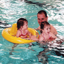 A father and twin toddler daughters enjoy a swim in the pool.
